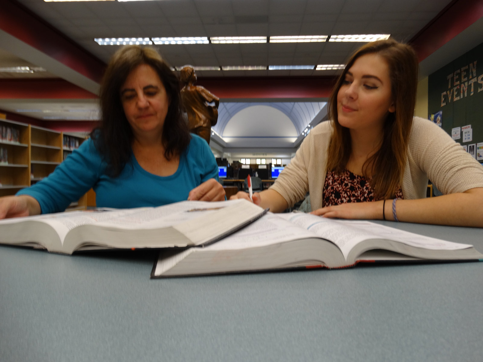 Anna reviewing a textbook with a college student in a library